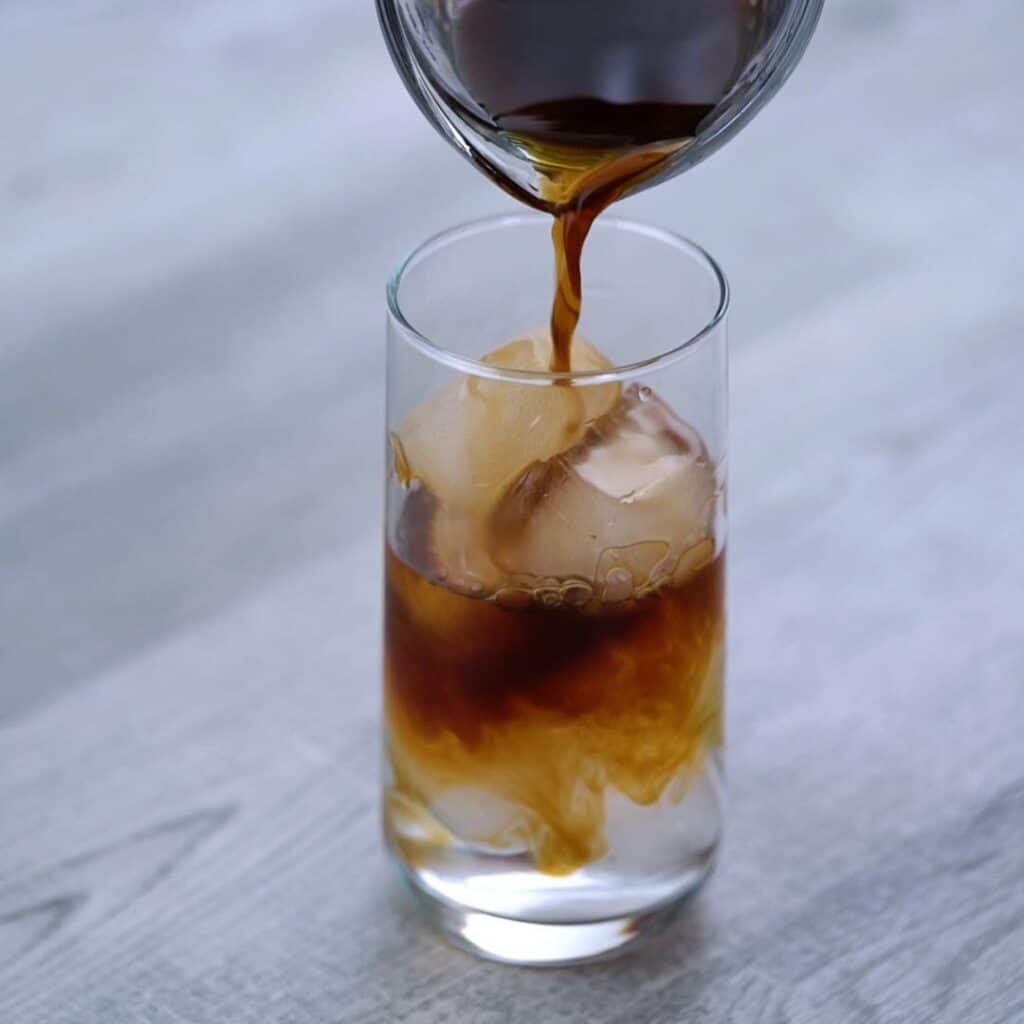 Pouring cold brew coffee over ice in to glass