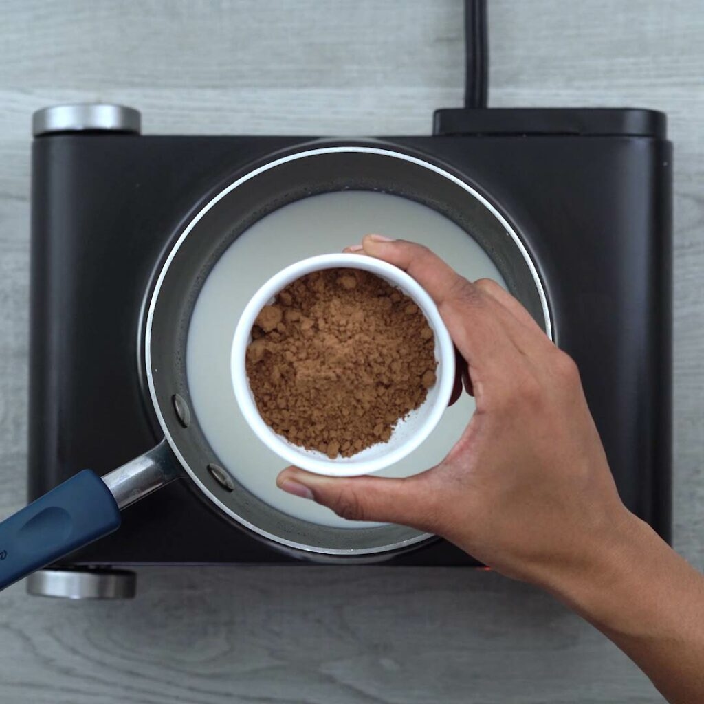 adding cocoa powder to milk in a sauce pan