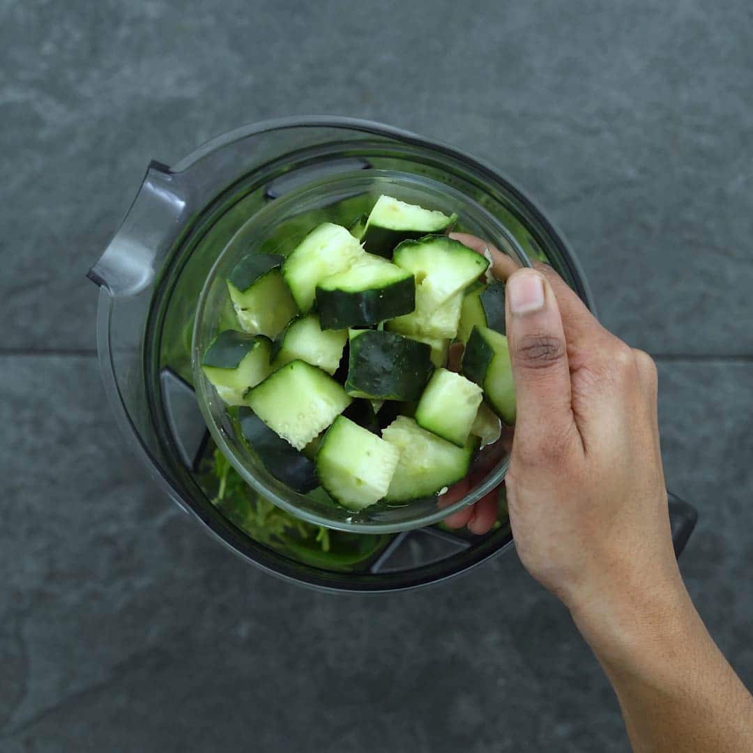Adding cucumber into the blender greens and fruits
