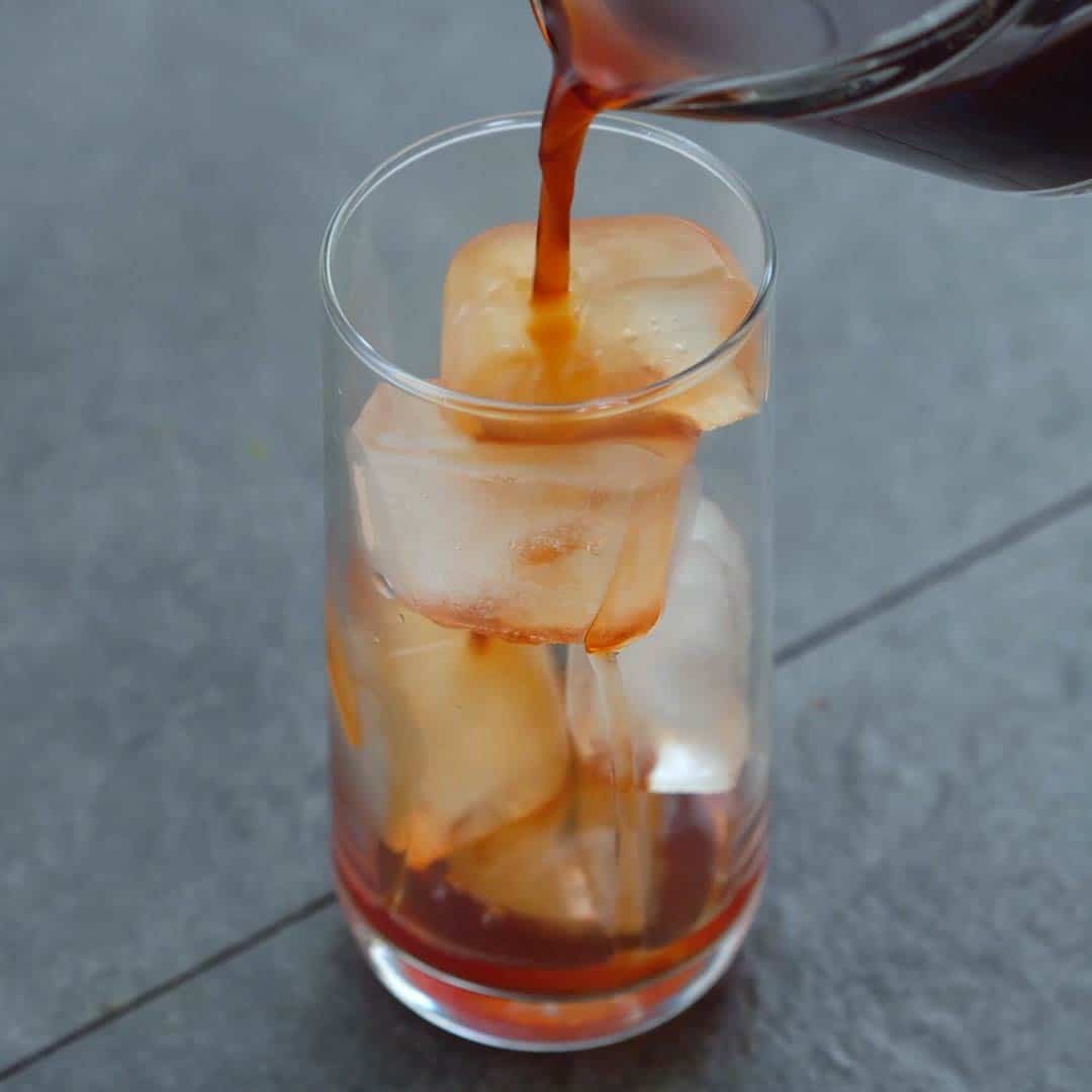 pouring Thai tea into a ice filled serving glass