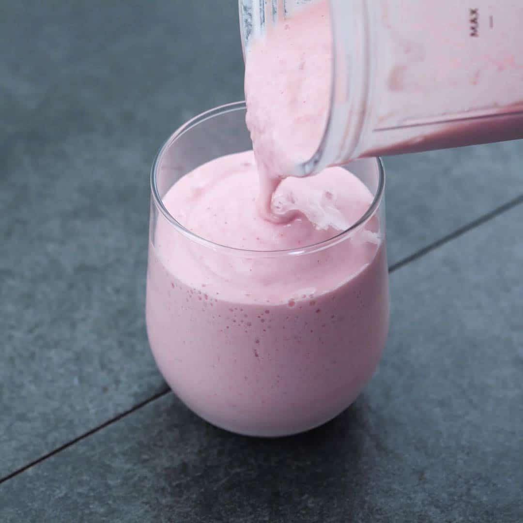 Pouring strawberry smoothie into serving glass