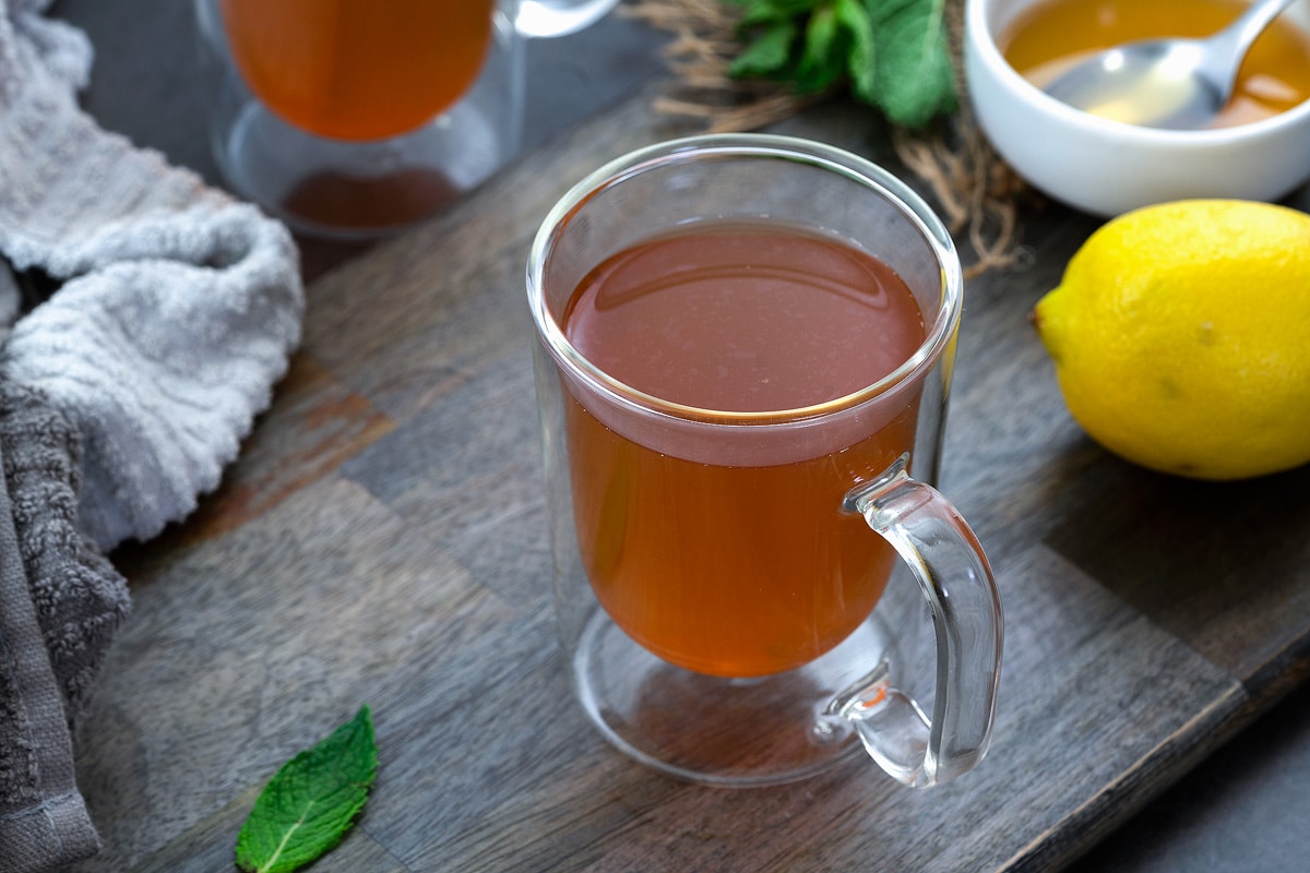 Mint tea in a serving glass with honey and lemon nearby