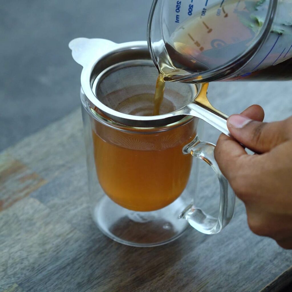 Filtering a green mint tea into a serving cup