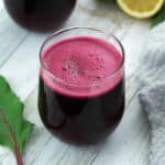Beetroot juice in glass placed on a whiteboard with lemon and beet leaf alongside