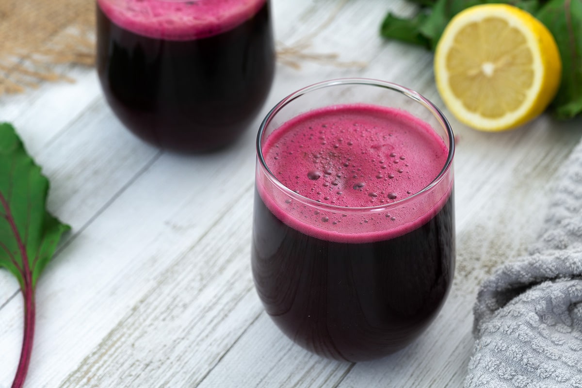 Beetroot juice in glass placed on a whiteboard with lemon and beet leaf alongside