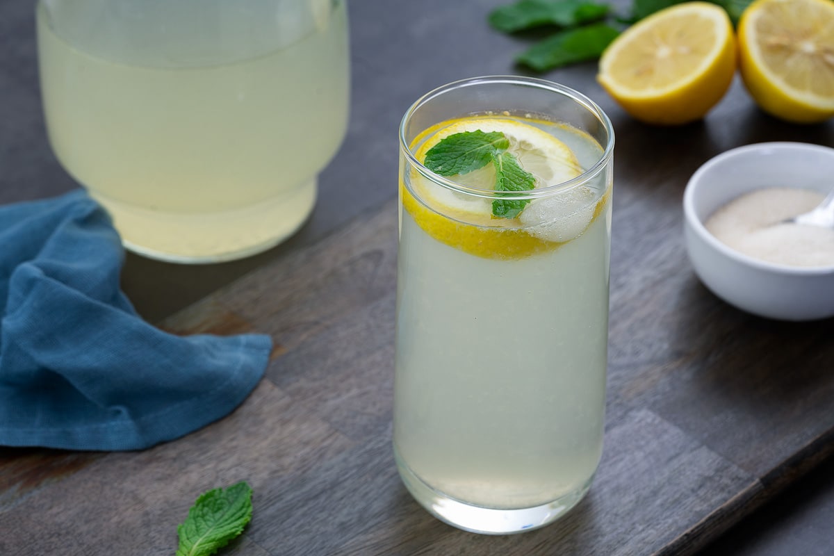 Fresh Lemon Juice in a glass placed on a grey table with sugar and cut lemon alongside