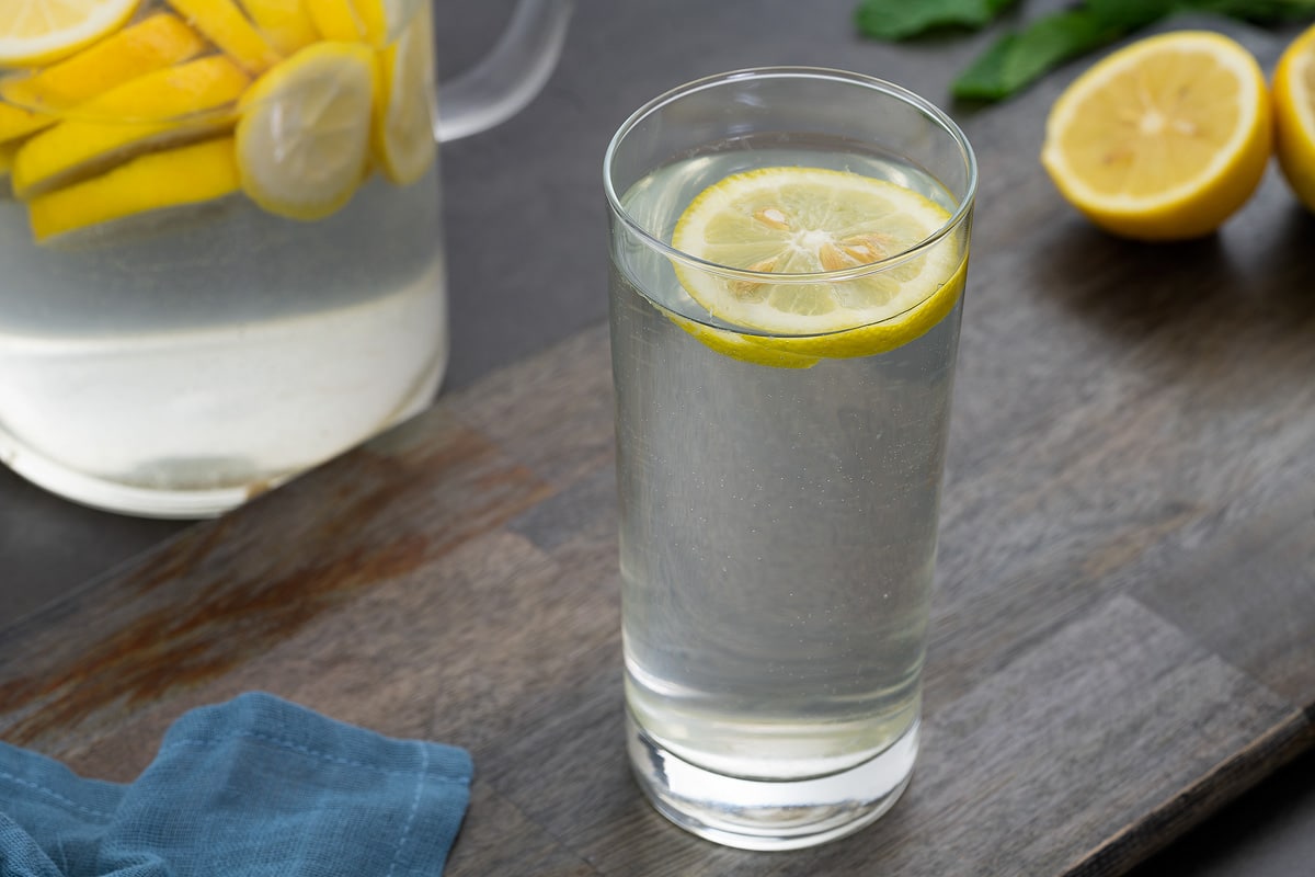 Lemon water in a glass with cut lemon on a grey table