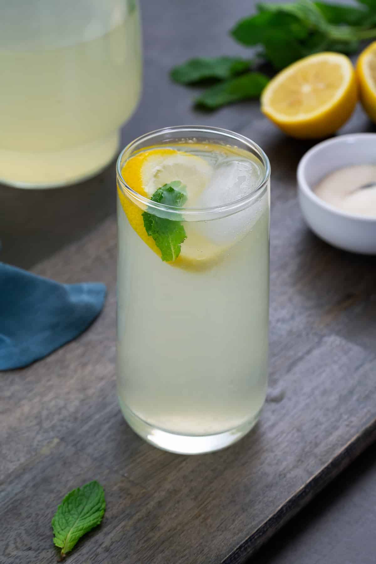 Fresh Lemon Juice in a glass placed on a grey table with sugar and cut lemon alongside