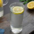 Lemon water in a glass with cut lemon on a grey table