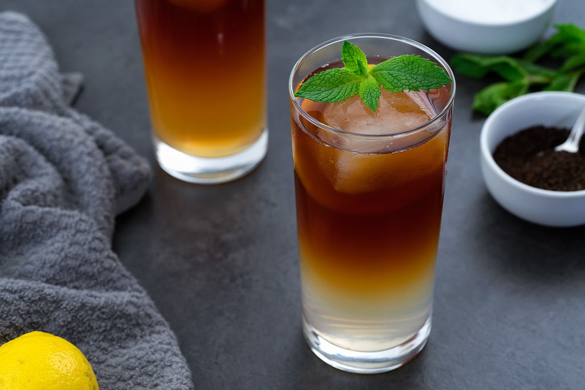 Arnold Palmer drink in a glass placed on a grey table with few ingredients around